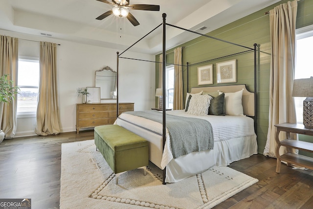 bedroom with dark wood-style floors, a tray ceiling, wood walls, and visible vents