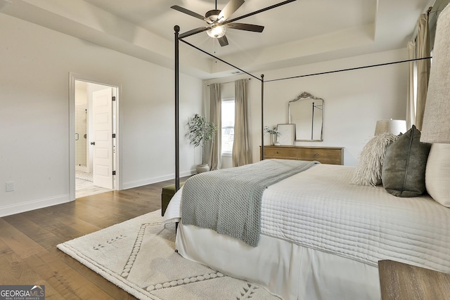 bedroom featuring a tray ceiling, connected bathroom, baseboards, and wood finished floors