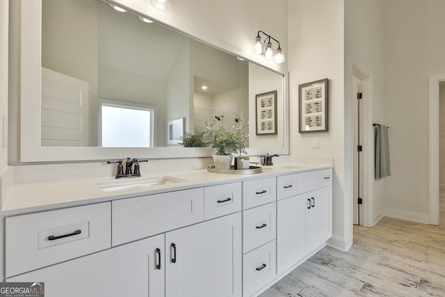 bathroom featuring double vanity, wood finished floors, a sink, and baseboards