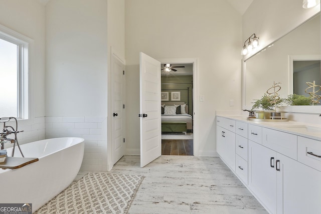 full bath featuring double vanity, tile walls, ensuite bath, a freestanding tub, and a sink