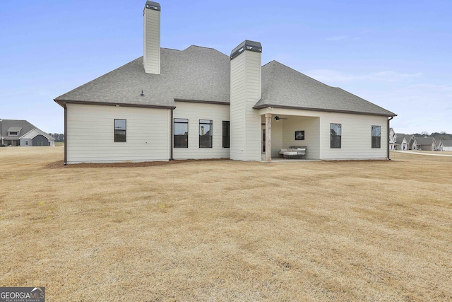 rear view of house featuring a yard, a shingled roof, a chimney, and a patio area