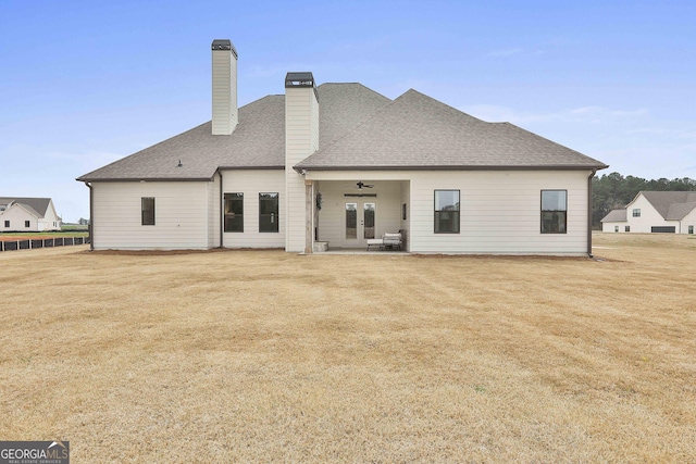 rear view of house with roof with shingles, a lawn, a chimney, and a ceiling fan