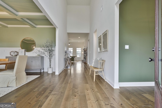 foyer entrance with coffered ceiling, wood finished floors, a towering ceiling, baseboards, and beam ceiling