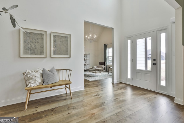 entrance foyer featuring a towering ceiling, an inviting chandelier, baseboards, and wood finished floors