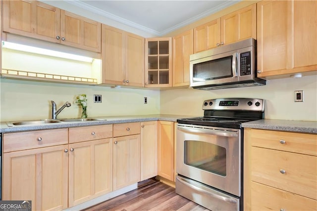 kitchen featuring ornamental molding, glass insert cabinets, stainless steel appliances, light brown cabinetry, and a sink