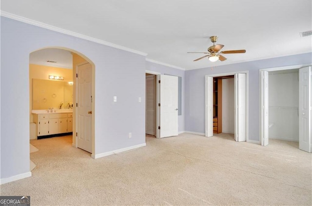 unfurnished bedroom with arched walkways, baseboards, two closets, and light colored carpet