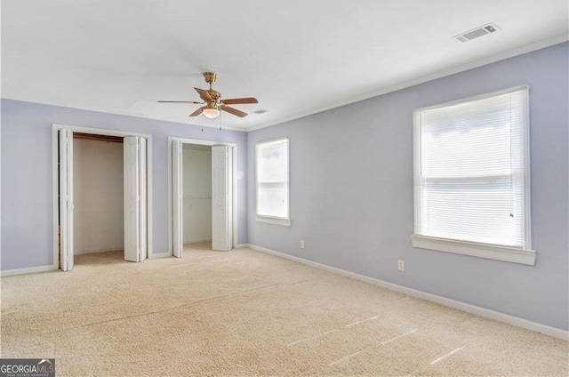 unfurnished bedroom with baseboards, two closets, visible vents, and light colored carpet