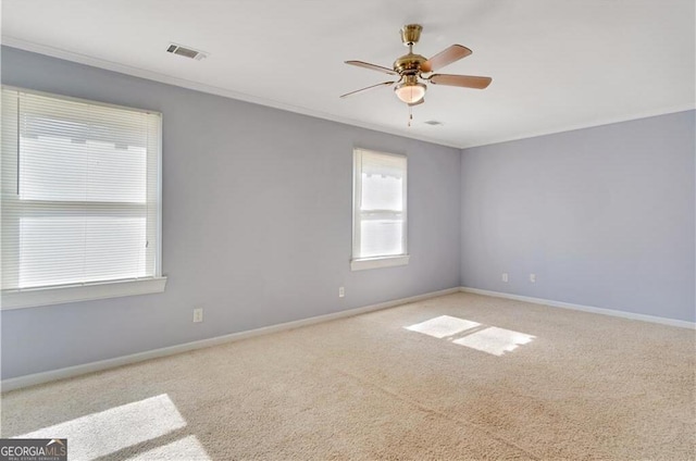 spare room featuring light colored carpet, visible vents, ornamental molding, a ceiling fan, and baseboards