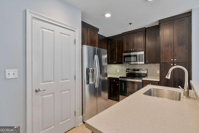 kitchen with tasteful backsplash, appliances with stainless steel finishes, light countertops, dark brown cabinets, and a sink