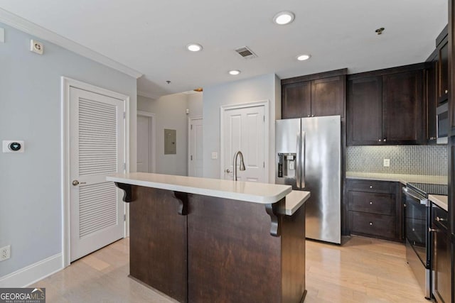 kitchen featuring appliances with stainless steel finishes, light countertops, a kitchen island with sink, and a breakfast bar