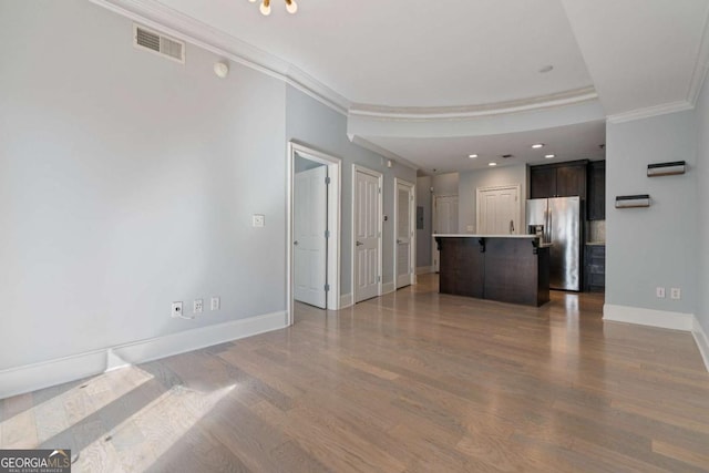 unfurnished living room with ornamental molding, wood finished floors, visible vents, and baseboards