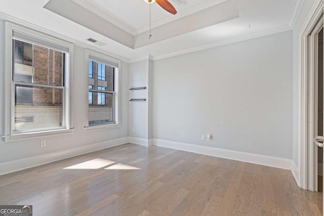 unfurnished room featuring light wood-style flooring, visible vents, baseboards, a raised ceiling, and crown molding