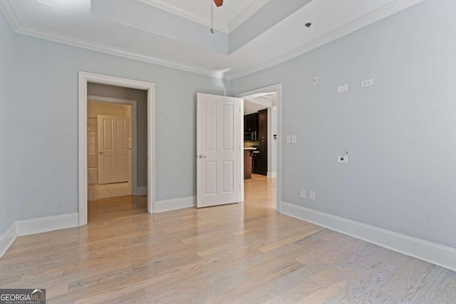 empty room featuring light wood-type flooring, baseboards, a tray ceiling, and crown molding