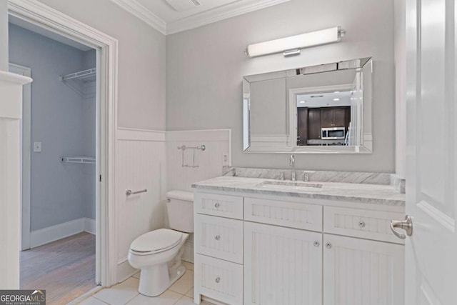 bathroom featuring wainscoting, toilet, ornamental molding, a walk in closet, and vanity