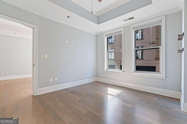 empty room featuring crown molding, a raised ceiling, visible vents, wood finished floors, and baseboards