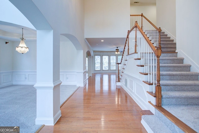 foyer entrance featuring stairway, arched walkways, light wood-style floors, a decorative wall, and ceiling fan with notable chandelier