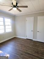 spare room featuring dark wood-style floors, baseboards, a ceiling fan, and crown molding