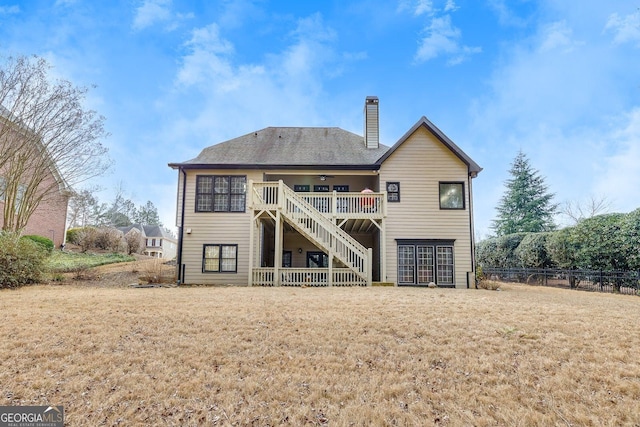 back of property with fence, a ceiling fan, stairs, a lawn, and a chimney