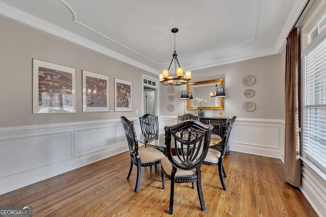 dining space with a chandelier, wood finished floors, visible vents, and crown molding