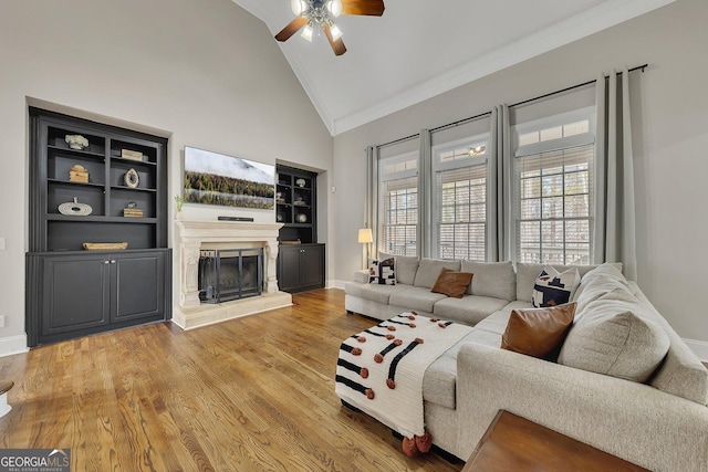 living room with a fireplace with raised hearth, high vaulted ceiling, wood finished floors, and baseboards