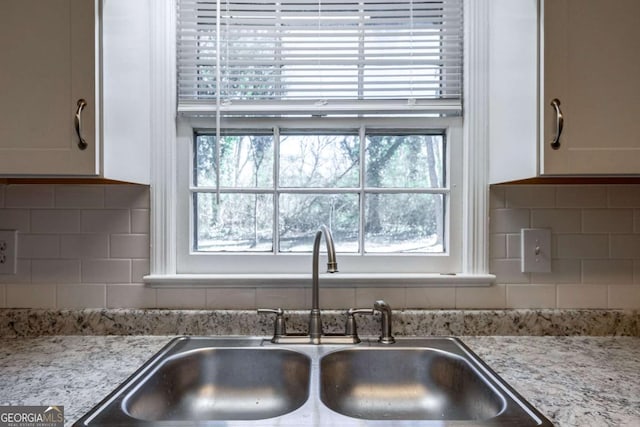 kitchen featuring tasteful backsplash, a sink, white cabinetry, and light stone countertops