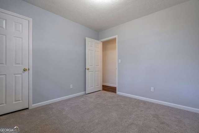 spare room featuring light carpet, baseboards, and a textured ceiling