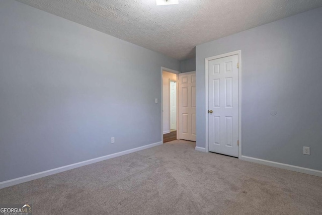 spare room with light colored carpet, a textured ceiling, and baseboards