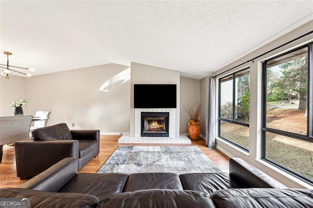 living area with a fireplace, light wood finished floors, lofted ceiling, a textured ceiling, and a chandelier