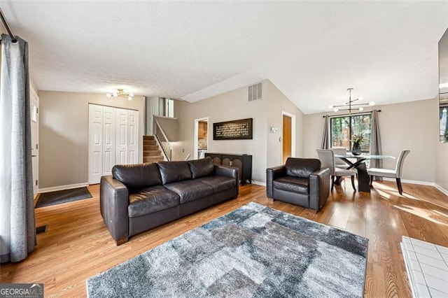 living area with stairs, wood finished floors, visible vents, and an inviting chandelier