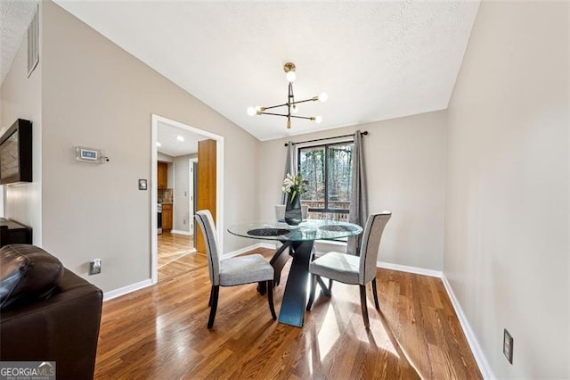 dining area with vaulted ceiling, baseboards, wood finished floors, and an inviting chandelier