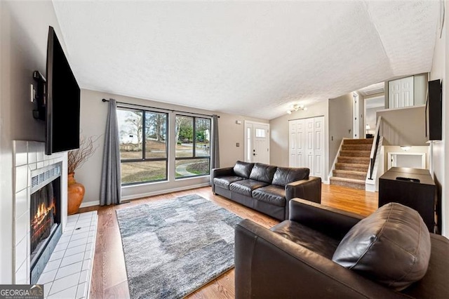 living area featuring vaulted ceiling, a textured ceiling, a tiled fireplace, and stairs