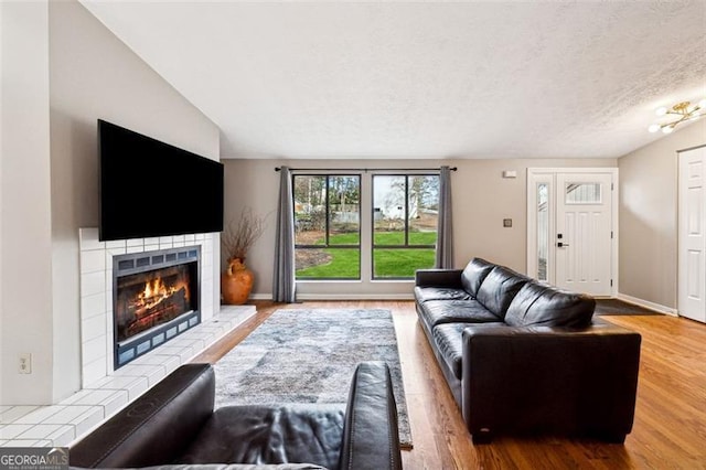 living room with baseboards, a textured ceiling, a tiled fireplace, and wood finished floors