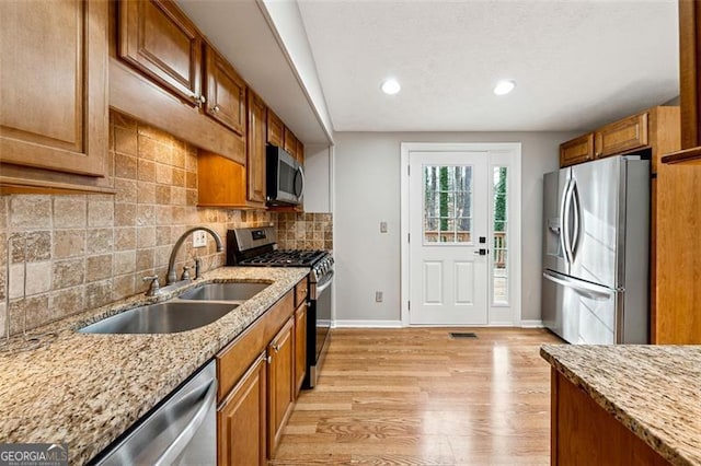 kitchen featuring appliances with stainless steel finishes, brown cabinets, a sink, and light stone countertops