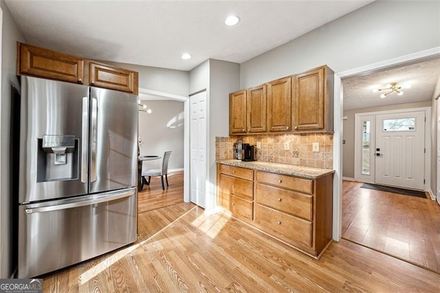 kitchen featuring light wood finished floors, baseboards, decorative backsplash, stainless steel refrigerator with ice dispenser, and recessed lighting