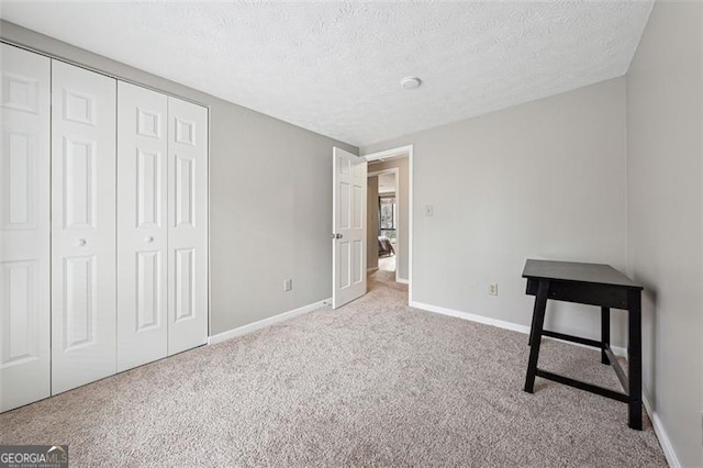 unfurnished bedroom with a closet, baseboards, a textured ceiling, and light colored carpet