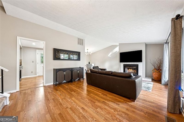 living room featuring visible vents, wood finished floors, a lit fireplace, vaulted ceiling, and a textured ceiling