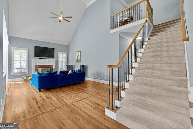 living area featuring wood finished floors, high vaulted ceiling, a ceiling fan, and stairs