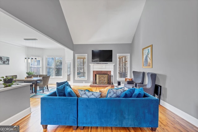 living room with high vaulted ceiling, a fireplace, light wood-style floors, and baseboards