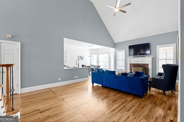 living room featuring a brick fireplace, a wealth of natural light, light wood-type flooring, a ceiling fan, and high vaulted ceiling