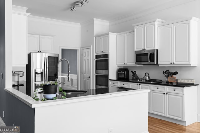 kitchen featuring stainless steel appliances, dark countertops, light wood-style floors, white cabinets, and a peninsula