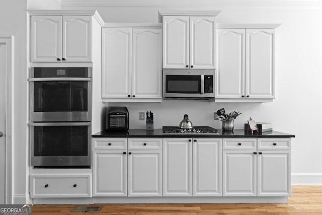 kitchen featuring appliances with stainless steel finishes, light wood finished floors, dark countertops, and white cabinetry
