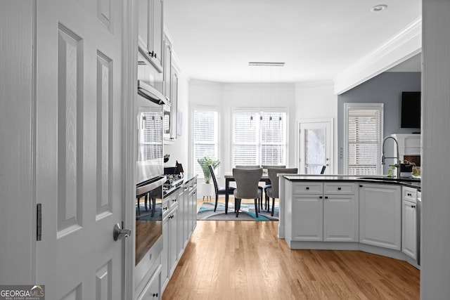 kitchen featuring white cabinets, dark countertops, ornamental molding, light wood-style floors, and stainless steel oven