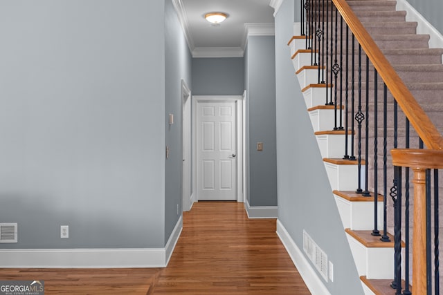 stairway with baseboards, visible vents, wood finished floors, and ornamental molding