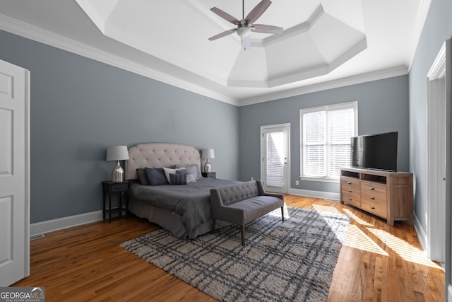 bedroom with ornamental molding, light wood-style flooring, a raised ceiling, and baseboards