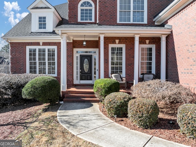 view of exterior entry featuring brick siding, a porch, and a shingled roof