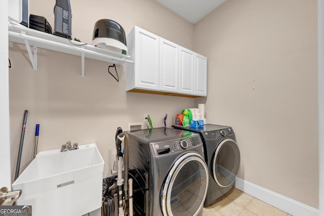 washroom featuring light tile patterned flooring, washing machine and dryer, a sink, baseboards, and cabinet space