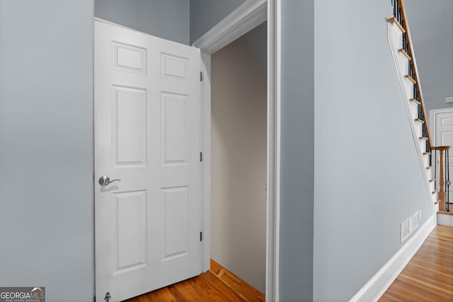 hallway with light wood-type flooring, stairway, baseboards, and visible vents