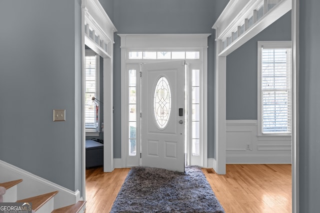 foyer entrance featuring light wood finished floors, wainscoting, visible vents, and a decorative wall