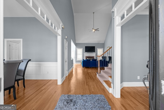 entryway with high vaulted ceiling, ceiling fan, a fireplace, stairs, and light wood finished floors