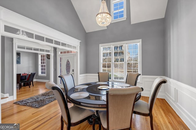 dining room featuring an inviting chandelier, vaulted ceiling, wood finished floors, and a wainscoted wall